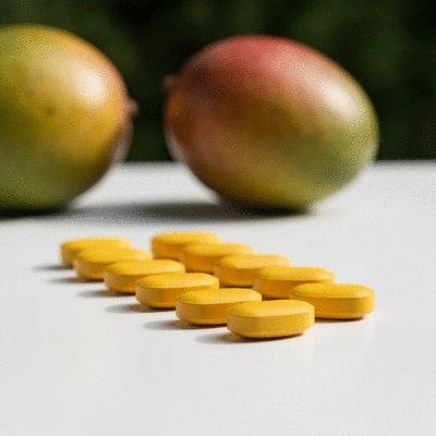 African mango pills on a clean white surface with fresh African mango fruit in the background